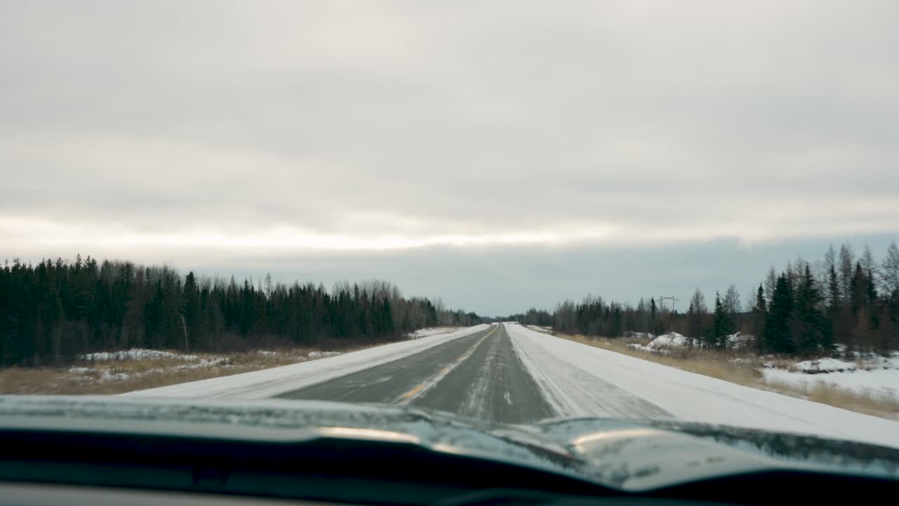 Car Mounted Camera Driving Shot Overcast Sky Down a Winter highway Forest Arctic Landscape Seen Through a Windshield near Thompson Manitoba Canada