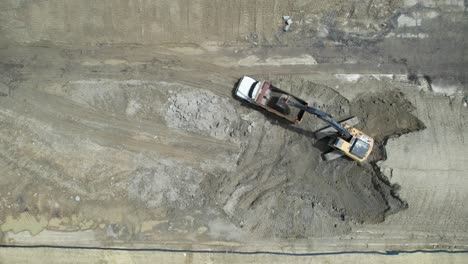 aerial view of a tractor filling a dumper truck with soil at construction site, project in progress