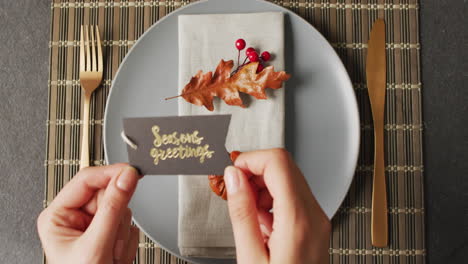 video of hands putting card with greeting on plate with autumn decoration lying on wooden mat