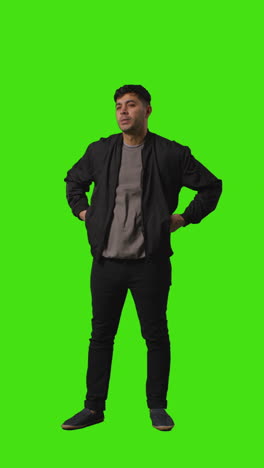 vertical video full length shot of casually dressed young man standing against green screen folding arms