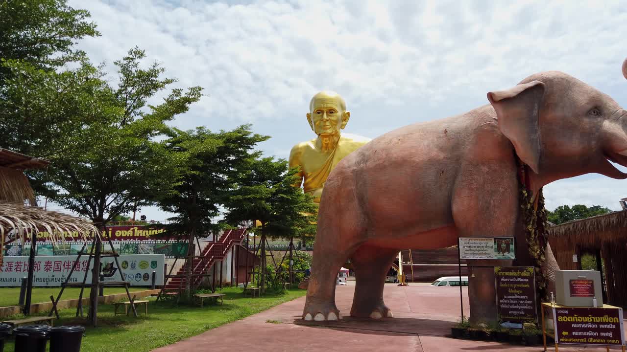 toma panorámica que muestra la estatua del monje dorado brillante luang pu thuat en el fondo y una escultura de elefante gigante en primer plano en el parque budista en phuttha utthayan maharat ayutthaya tailandia