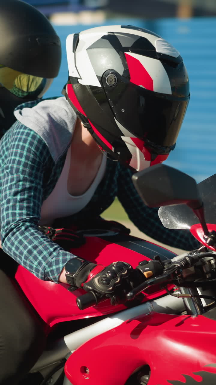 dos amigos montando una bicicleta eléctrica con sus cascos, pasando por un edificio blanco con dos coches negros estacionados cerca, el viento agita sus ropa mientras viajan, con un zinc azul visible