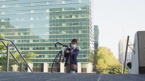 asian man wearing face mask carrying bicycle while climbing up the stairs at corporate park