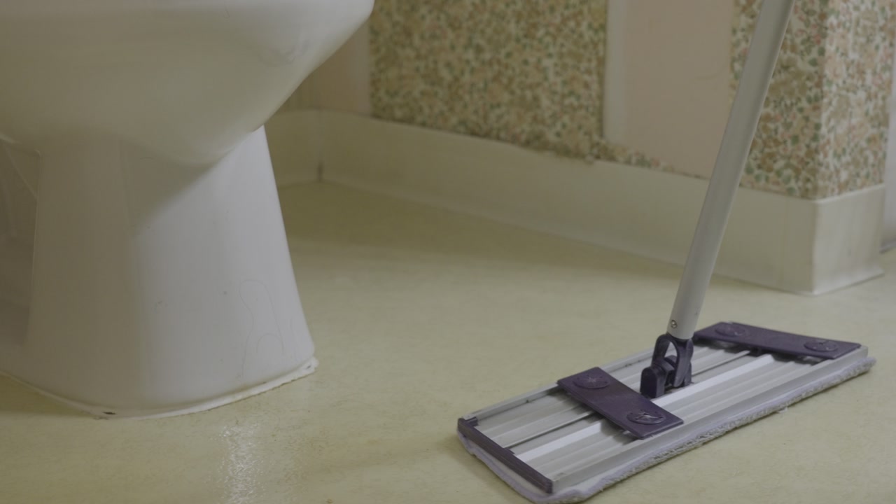 Slow motion clip of sweeping up a dirty bathroom floor.