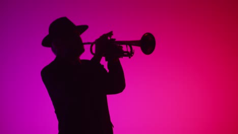 man plays music on trumpet in room flickering with different neon lights, front view. jazz performer in hat and suit plays trumpet