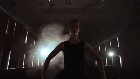 slow motion: prima ballet rehearses a solo performance standing on the stage of the theater in smoke in a black dress in the light.