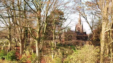 toma panorámica izquierda mirando a través de árboles sin hojas de otoño hasta el cementerio - iglesia en segundo plano
