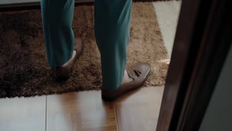 Groom-in-teal-trousers-and-brown-shoes,-standing-on-a-patterned-carpet,-highlighting-wedding-preparation