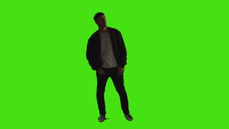 Full-Length-Shot-Of-Casually-Dressed-Young-Man-Standing-Against-Green-Screen-Waiting-With-Hands-In-Pockets-In-Low-Key-Lighting