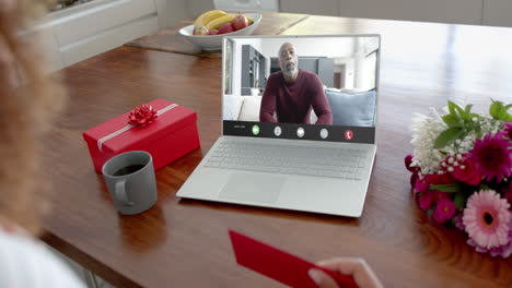 caucasian woman holding envelope and talking with african american man on laptop screen