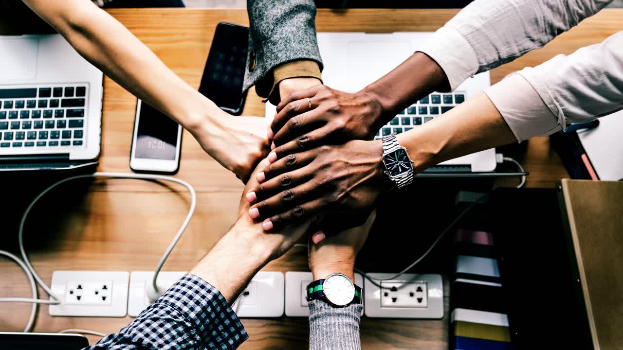 Top-down view of diverse hands fist-bumping over laptops, symbolizing teamwork and unity