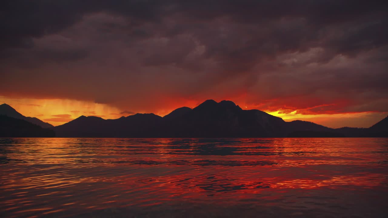 Scenic time-lapse video of a beautiful and romantic sunset at mountain lake Walchensee in Southern Germany - Bavaria with moving red evening clouds and calm waves in real time.