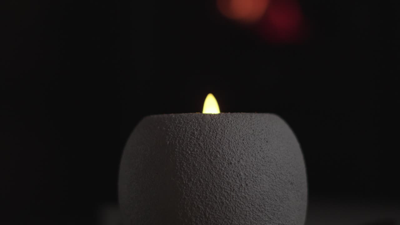 LED svíčka s bílým tělem na černém pozadí a světlem lampy nahoře