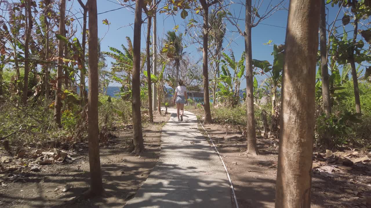 Young white beautiful woman exploring Bali Indonesia, walking between palms and searching for sandy beach and ocean.