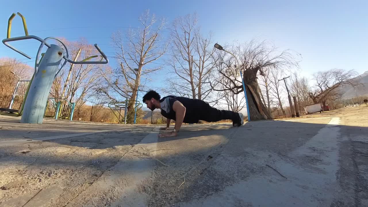 Fit man with a beard doing pushups at an outdoor park on a sunny day, static shot