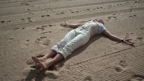 man relaxing on sand. man making angel on sand. man lying on sand