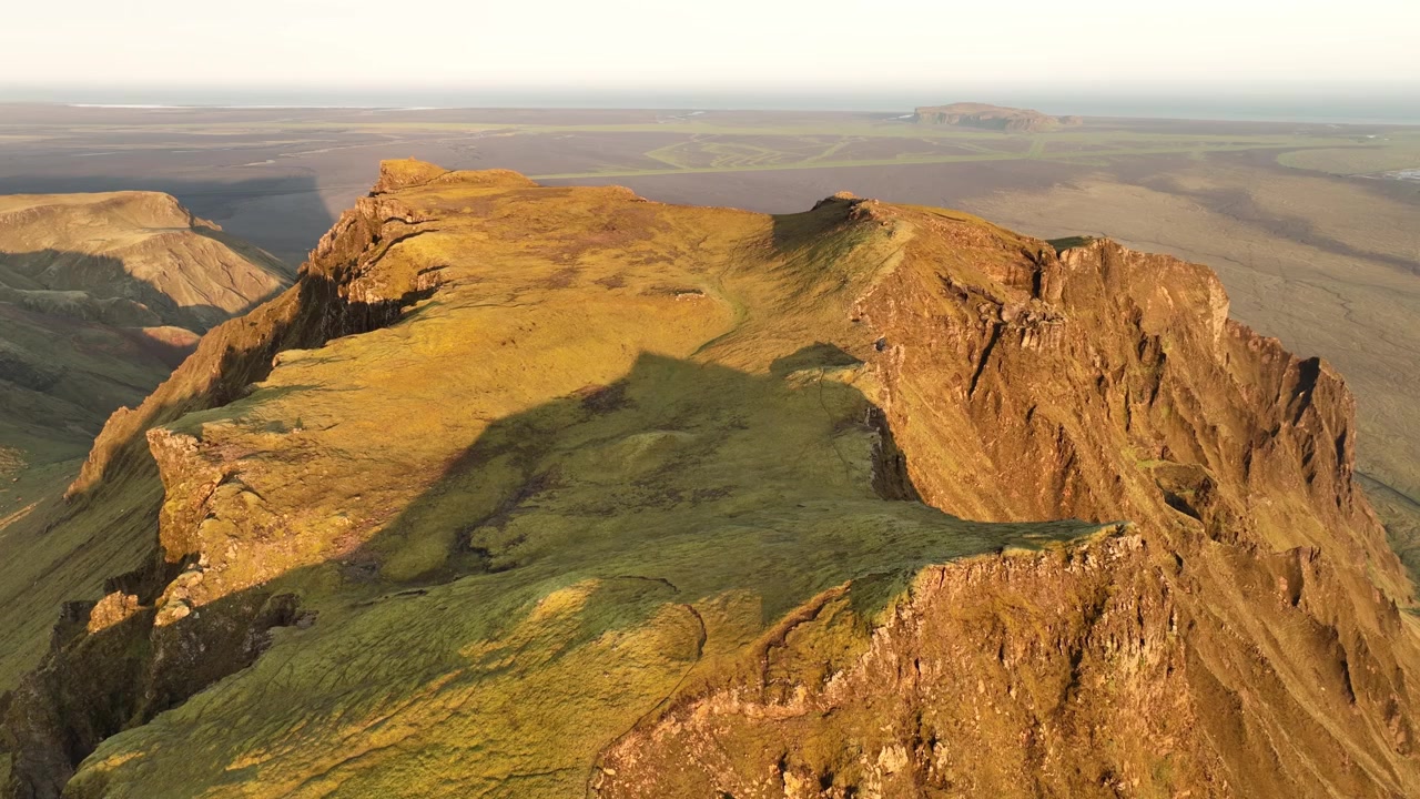 Veduta aerea di un'aspra cresta montuosa a Thakgil, Islanda, bagnata dalla luce dorata del tramonto, con vaste pianure sullo sfondo