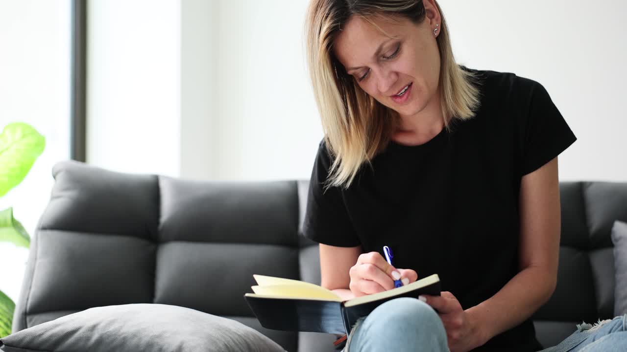 Woman writing in notebook on couch
