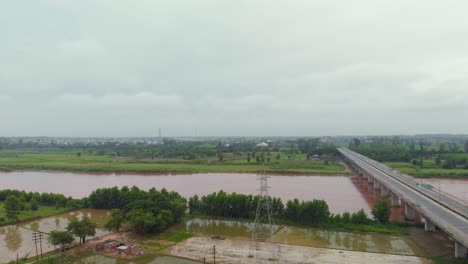 Vista-Aérea-Del-Paso-Elevado-Sobre-Tierras-Agrícolas-Cerca-Del-Río,-Y-El-Canal-Después-De-La-Lluvia-Con-Agua-Turbia-Lluviosa-Fuera-De-La-Ciudad-En-La-Región-De-Punjab,-India