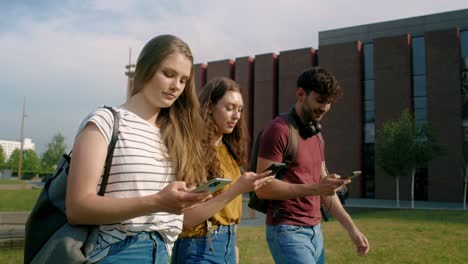 estudiantes universitarios caminando y navegando por los teléfonos junto al edificio del campus universitario.