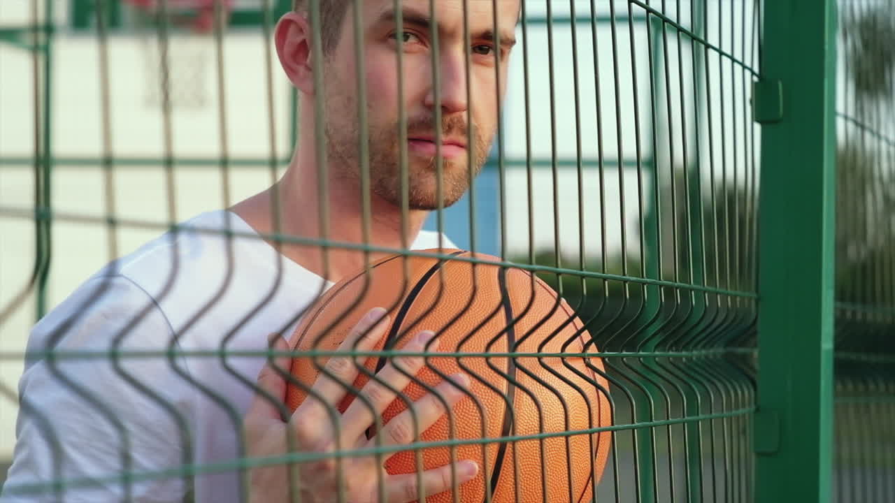 Homem segurando uma bola de basquete atrás de uma cerca