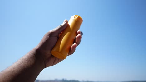 mano sosteniendo una botella de protector solar contra un cielo azul