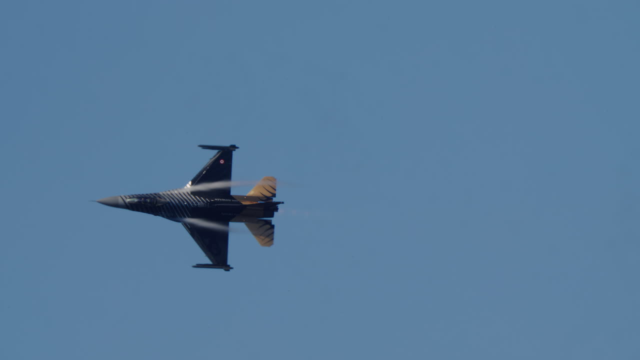 F-16 Kampfjet fliegt mit Kondensstreifen am blauen Himmel.