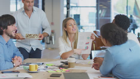 colleagues celebrating businesswoman's birthday at meeting around table in modern open plan office