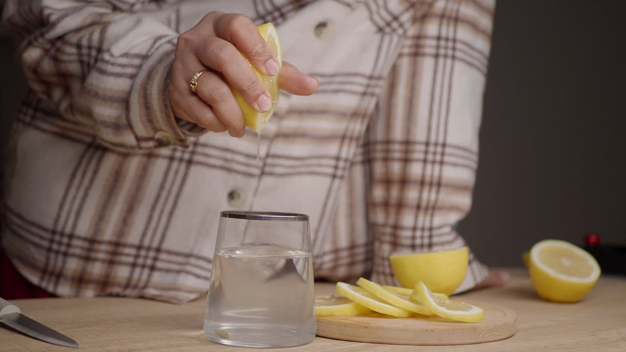 Persona exprimiendo limón fresco en un vaso de agua