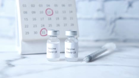 covid-19 vaccine vials and syringe on calendar background