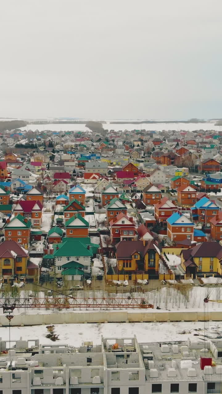 flight over residential cottage complex by gray ongoing building with yellow construction cranes on weekend