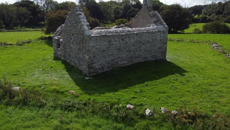 Establishing-aerial-view-ancient-Capel-Lligwy-ruined-chapel-on-Anglesey-island-coastline,-North-Wales