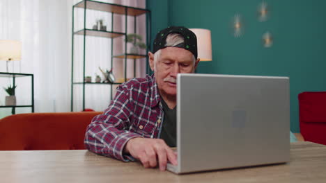 el abuelo mayor comienza a trabajar en la computadora portátil, envía mensajes, hace compras en línea en casa