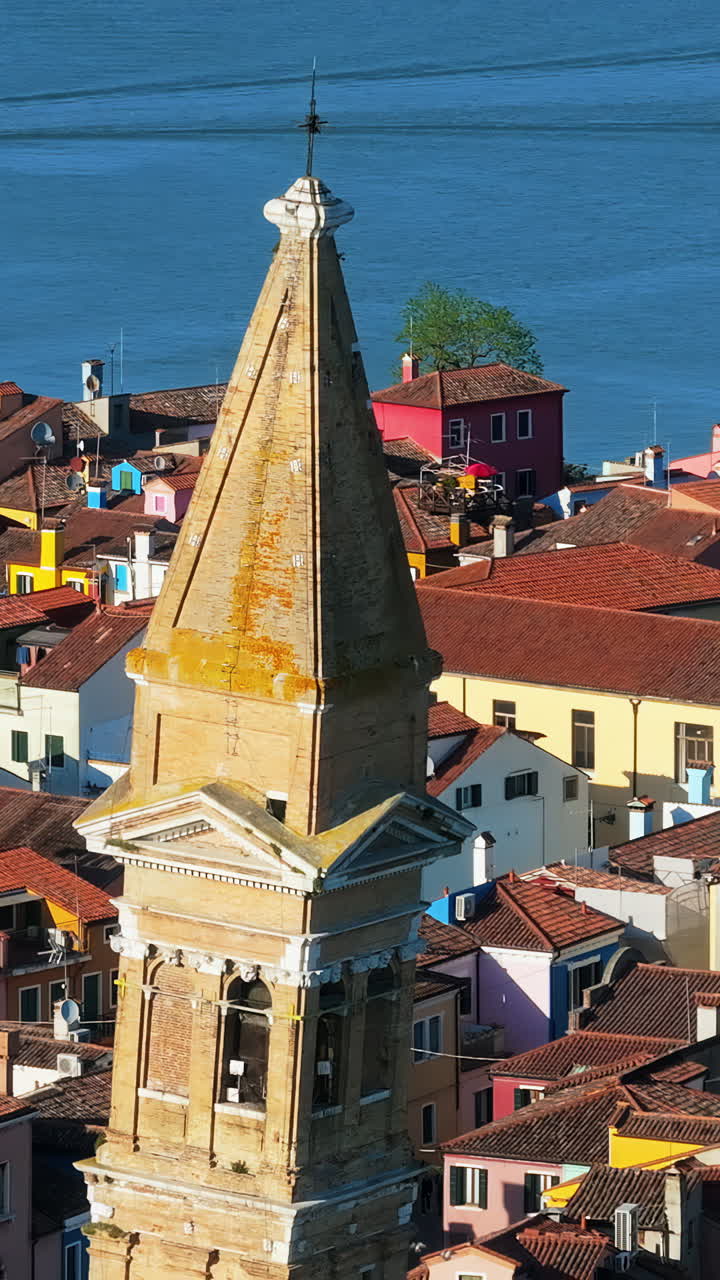 Aerial drone view of the Church of Saint Martin Bishop surrounded by colourful houses in Burano Island, Italy. Vertical