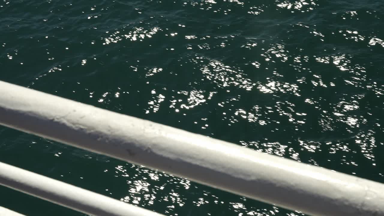 페리 교차로의 바 레일링을 통해 바라보는 가까운 시각, 바람이 작은 파도와 파동을 일으키면서 바다 물의 표면에서 선이 반이고 반인다