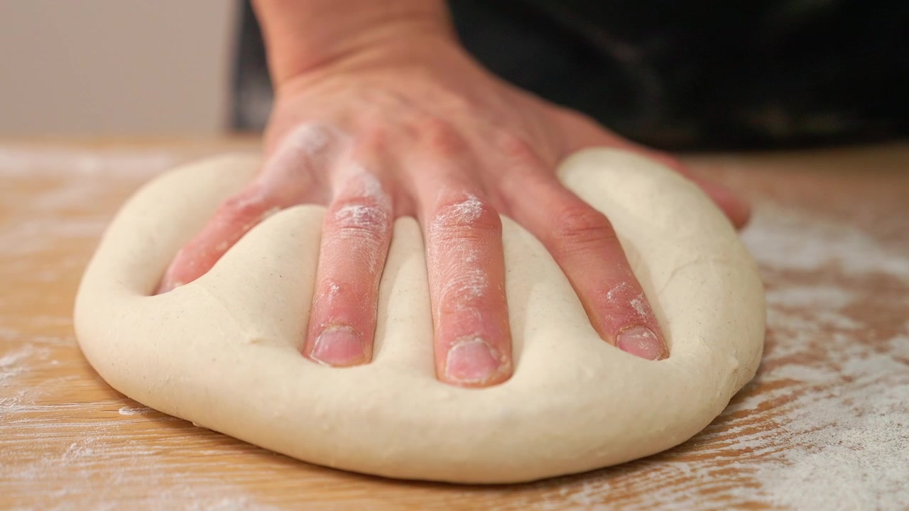 Close-Up of Hand Kneading Fresh Dough on a Floured Wooden Surface