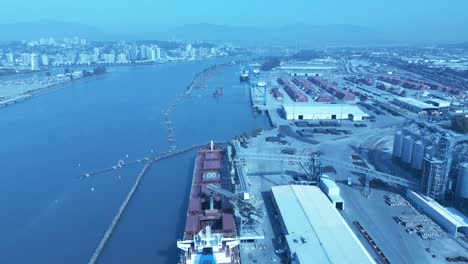 grain loading on freighter from distribution port canal in surrey bc canada top birds eye view overlooking commercial dock as other cargo ship are getting loaded with wood vehicles drone flyover 1-2