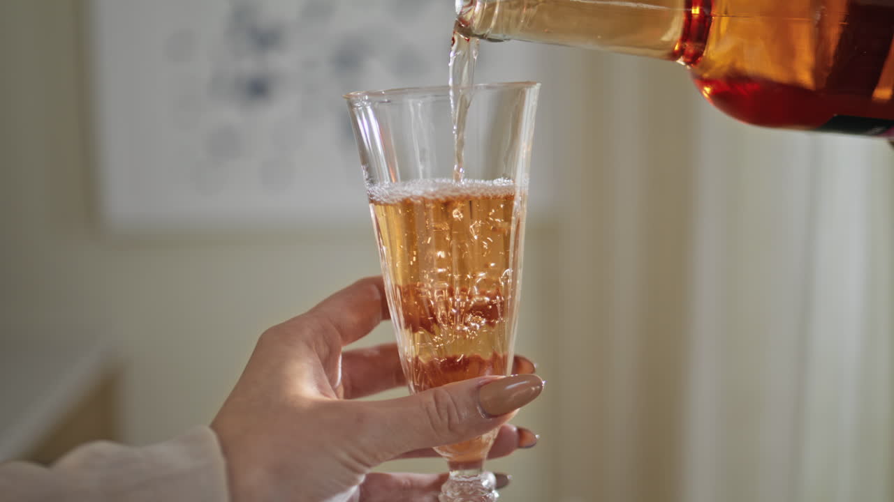 Alcohol drink flowing glass at home celebration closeup. Unrecognizable person