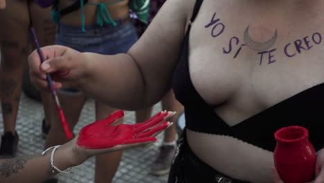female activist paints performer’s hand red as blood in representation of gender violence during women’s day peaceful protest
