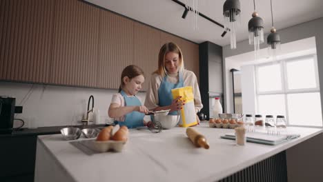 happy mother and child are cooking cake in home kitchen, sifting flour by sifter, zooming shot in apartment