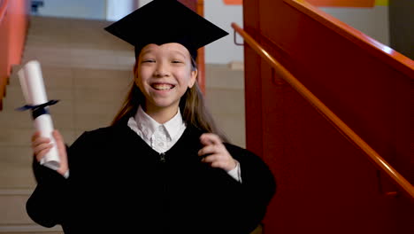 happy preschool female student in cap and gown holding diploma and celebrating her graduation