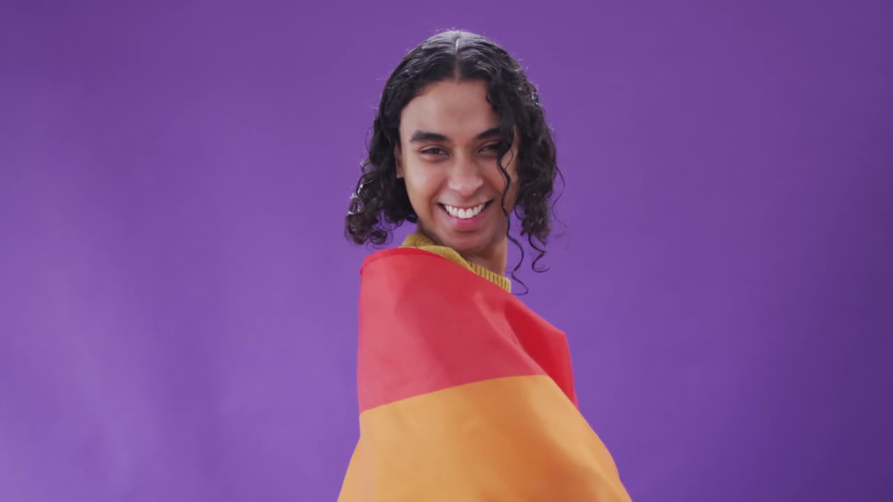 retrato de un feliz hombre biracial sosteniendo una bandera lgbt con los brazos abiertos