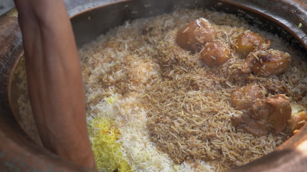 Nærbillede af en gademadssælger i Indien, der serverer frisk, dampende kyllingebiryani med basmatiris og kartofler fra en traditionel ler-handi.