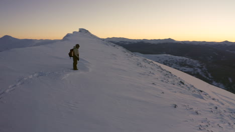 Aerial-cinematic-pan-to-right-featuring-snowboarder-atop-of-mountain-peak-reflecting-on-scenic-Mountain-View-during-late-sunset-mid-winter-Vail-Pass-Colorado