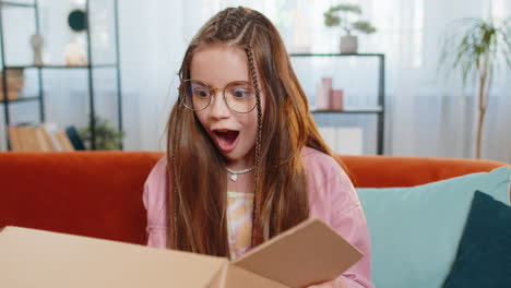 feliz asombrada chica con el pelo azotado por el viento desempaquetando apertura caja de cartón entrega paquete compra regalo