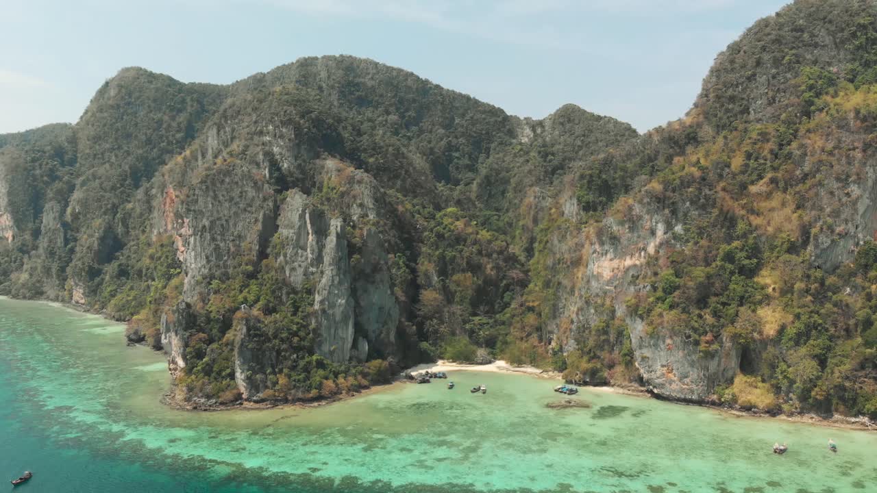 Vách đá vôi cao chót vót liền kề bờ biển xanh ngọc bích nông ở Vịnh Tonsai, Đảo Ko Phi Phi Don, Thái Lan - Cảnh quay trượt chậm từ trên không