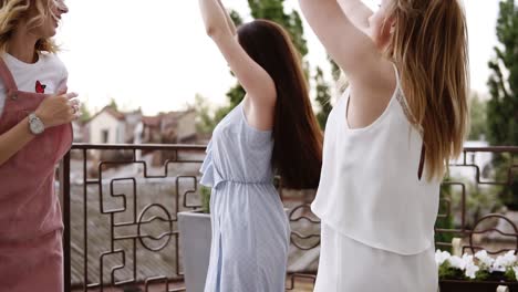 young women dance happily on the balcony. carefree moves. modern, stylish clothes. laughing and having fun. bright day on a balcony. slow motion