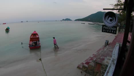 scuba tanks are loaded onto a long narrow boat for the morning dives. man carrying tanks from the beach in front of a dive shop. morning light on a peaceful beach in koh tao, thailand.