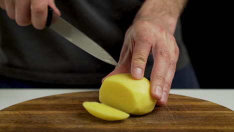 chef cutting and slicing peeled potato on chopping board, closeup