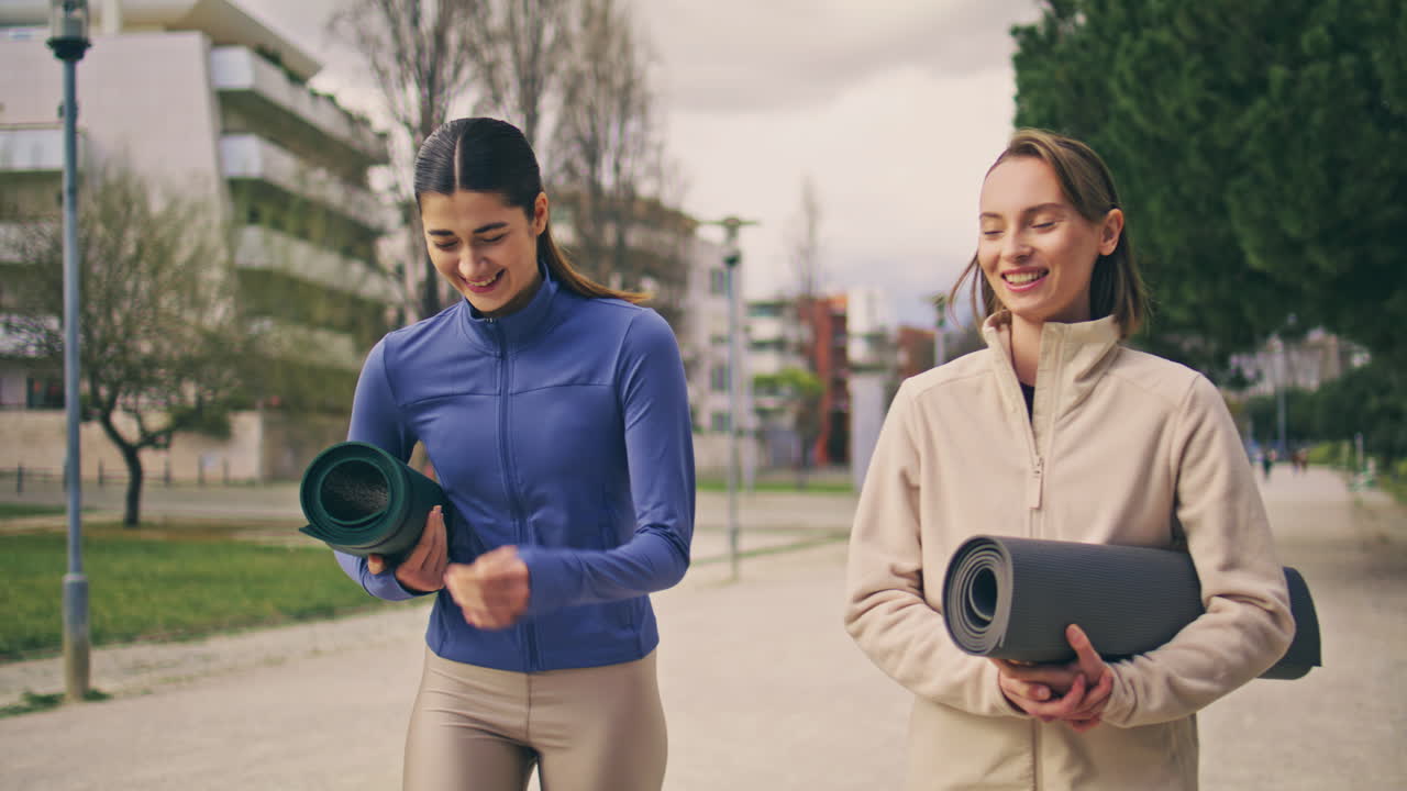 felices yogini hablando en la calle caminando juntos. riendo mujeres deportivas paseando por el callejón